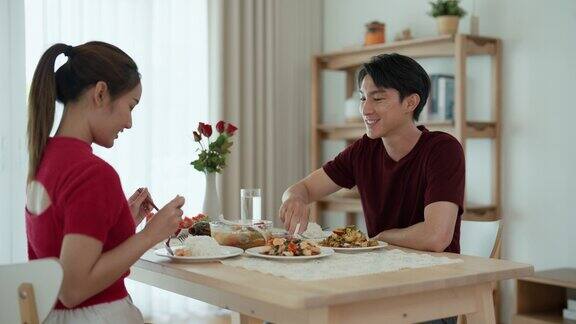 一个年轻的亚洲男子正在为他的女朋友舀食物两人一起在家里享用午餐