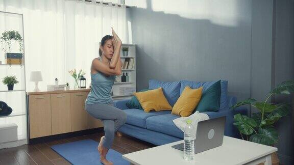 年轻有吸引力的亚洲妇女在运动服装观看健身在线视频在笔记本电脑练习瑜伽初学者在客厅在房子居家隔离锻炼和没有健身房的健身锻炼