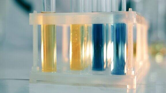 实验室里装有蓝色和黄色物质的试管在实验室工作一名实验室技术人员将试管放在三脚架上近景