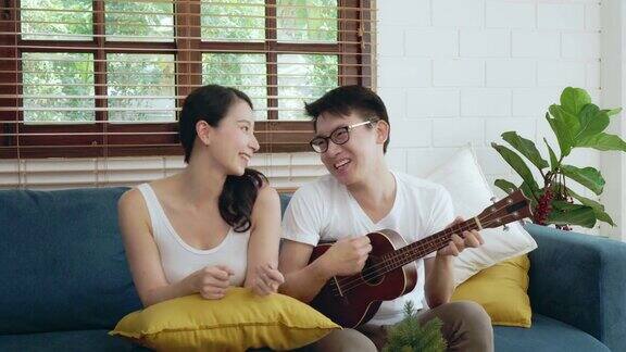 亚洲夫妇家庭在沙发上放松弹吉他和唱歌
