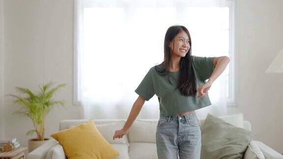 年轻的亚洲女子在家里客厅的地板上跳舞快乐亚洲女性微笑放松在家里健康的心理健康和幸福