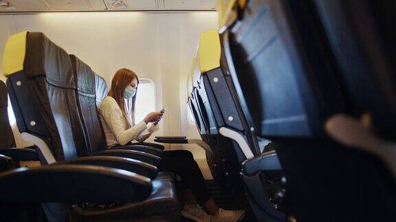 商界女性戴着口罩在飞机上使用手机