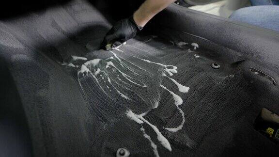 一名工人正在车里清洗地毯用刷子擦泡沫手拿着黑色橡胶手套特写