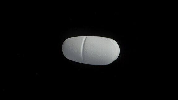 一个白色的大药丸在黑色的背景上旋转极端特写镜头前视图极端特写镜头