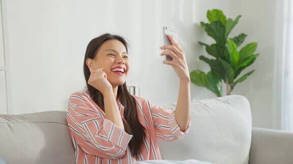 亚洲美女在客厅用手机视频通话年轻美丽的女孩感觉快乐和放松享受在家里用智能手机在线虚拟通话科技生活方式