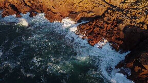 日落时分无人机拍摄的海浪冲击棕色岩石悬崖的景观