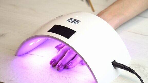 女孩将手放在指甲油固化灯下等待指甲油变硬紫外线指甲灯