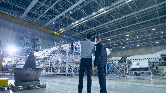 飞机维修机械师和总工程师在大型飞机研发设施中进行讨论