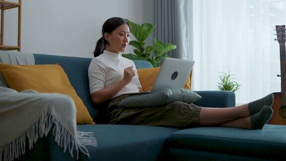 亚洲女性坐在家里的客厅里用笔记本电脑进行视频通话