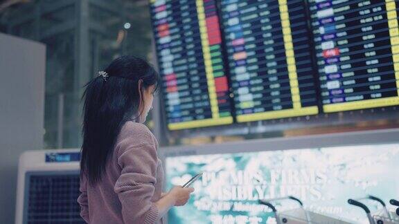 一名亚洲女子在机场航站楼用智能手机查看航班时刻表