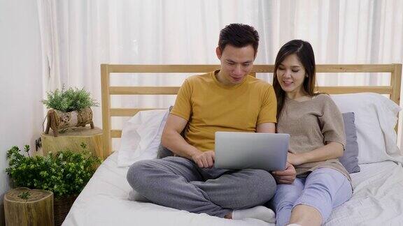 年轻的亚洲幸福夫妇使用笔记本电脑在卧室夫妇放松和花时间在一起在家里