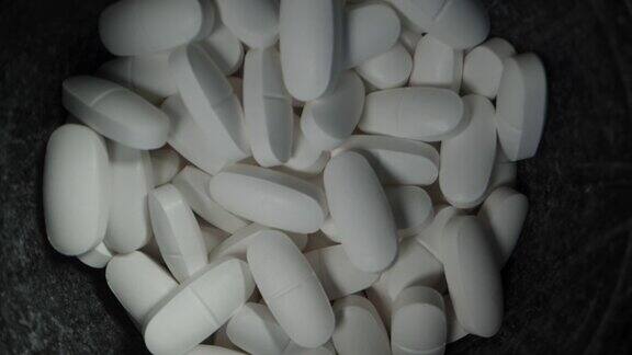 一个黑色的罐子上面有白色的药片在黑色的背景上旋转多莉滑块极端特写前视图