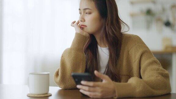 使用智能手机的年轻亚洲女性亚洲女性在家思考和孤独