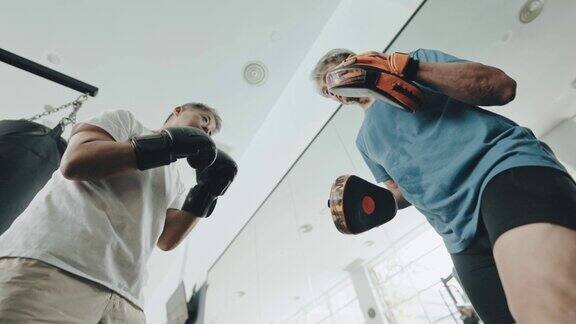低角度亚洲华人高级男子练习拳击陪练在健身房例行的周末活动