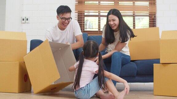 韩国的妈妈、爸爸和女儿在搬家后的新家拆行李时一起玩一起拿着箱子坐在地板上
