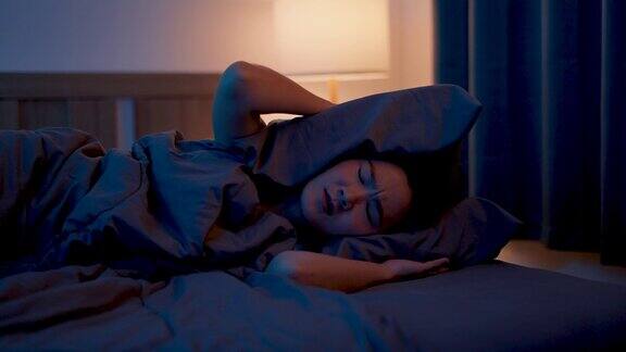 亚洲女性对噪音感到厌烦失眠躺在卧室的床上捂着耳朵