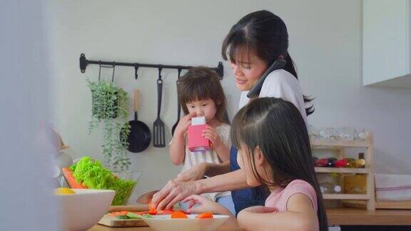 亚洲忙碌的母亲打电话和女儿在厨房做饭幸福的家庭爱美丽的父母妈妈和小妹妹感到幸福享受在家里的时间健康食品