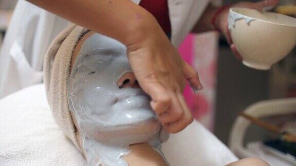 年轻的亚洲女性应用维生素面膜头部按摩在水疗中心