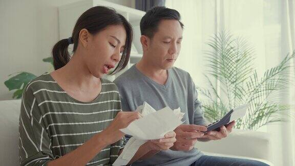 亚洲夫妇用计算器计算水电费计算支票信用卡收据每月开支账单一起坐在家里客厅的沙发上生活方式花时间在家里