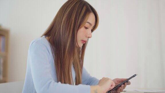 快乐的年轻亚洲女人放松在舒适的家里在智能手机上打字聊天信息微笑的女孩用手机聊天在浏览器上搜索信息无线互联网网上购物