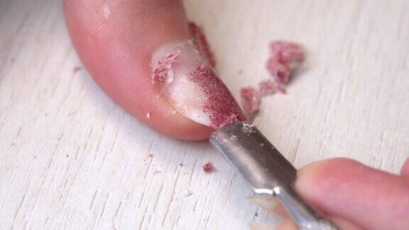 用刮刀刮掉旧的指甲油独有的美甲服务美甲师用粉红色的凝胶指甲油涂指甲修剪整齐的粉红色的指甲指甲油的应用程序