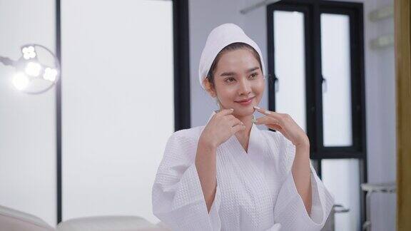 快乐可爱的亚洲妇女在白色浴衣举起手臂摆姿势在美容诊所的肖像年轻美丽的亚洲妇女在浴衣和毛巾包裹头部微笑与自然健康的皮肤