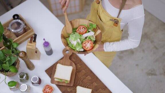 快乐的年轻亚洲女性喜欢有趣的舞蹈拿着木制沙拉勺做饭用叉子唱歌女性在厨房柜台边笑边在家里准备素食健康食品