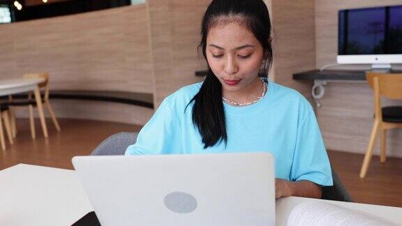 亚洲年轻少女在学校图书馆使用笔记本电脑打字高校图书馆教育与学生学习理念