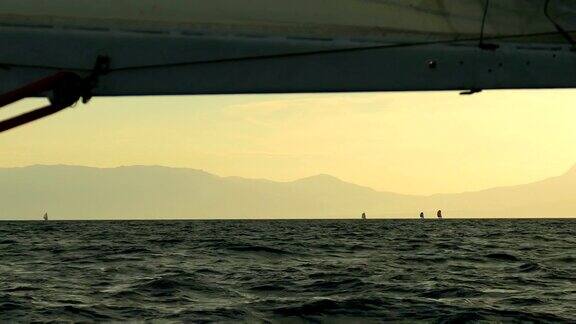 帆船赛在日落对山的海岸线的背景