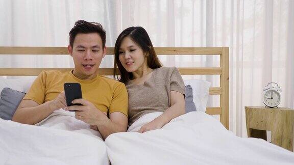年轻的亚洲幸福夫妇在卧室使用手机夫妇放松和花时间在一起在家里