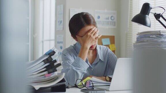 尝试年轻的亚洲办公室员工感觉不舒服有一个头疼的长时间工作在办公室