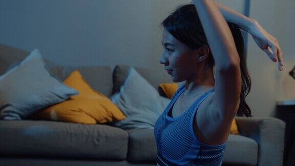 年轻的亚洲女士穿着运动服做瑜伽练习晚上在家里的客厅里锻炼