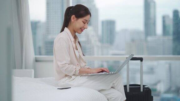 亚洲女商人用科技笔记本电脑在床上工作而在市中心带着行李箱进入房间或办公室