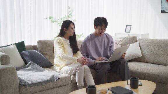 一对韩国夫妇在他们时髦的家中分享微笑年轻英俊的男人和迷人的女人用笔记本电脑与朋友在社交媒体上进行虚拟游戏之夜静态的画面