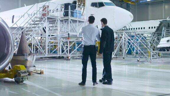 飞机维修机械师和总工程师在大型飞机研发设施中进行讨论咨询图纸他们分析、检查、开发和设计飞机
