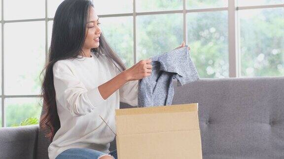 满意的亚洲女性顾客坐在沙发上打开网上订购购物快递包裹开心的年轻女子打开包好购送货上门