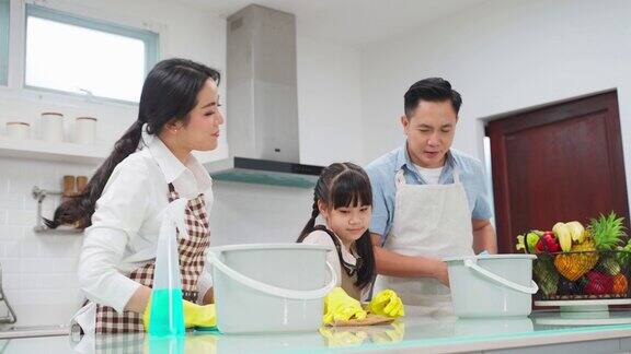 亚洲年轻家庭教他们的女儿清洁厨房柜台孩子和父母一起跳舞一起笑很开心可爱的家庭在快乐的打扫房间时的快乐时刻