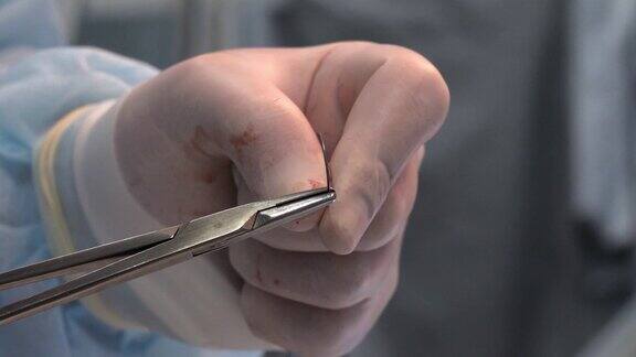 外科医生用带着血迹的医用手套的手取出针线医生正准备缝合手术切口概念的结束操作