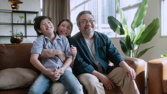 幸福甜蜜的亚洲家庭爸爸妈妈和儿子一起坐在沙发上看电视笑着微笑的亚洲家庭在家里隔离隔离时刻处于封锁状态