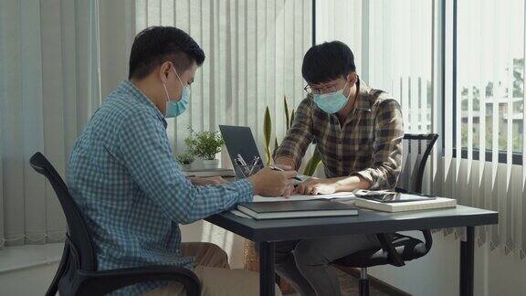 在新冠肺炎疫情期间亚洲同事戴着口罩在办公室工作