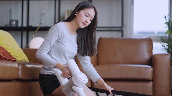 穿着t恤和短裤的亚洲年轻美女正在家里明亮舒适的房间里用吸尘器清洁地毯她用的是现代无绳吸尘器电器和有趣