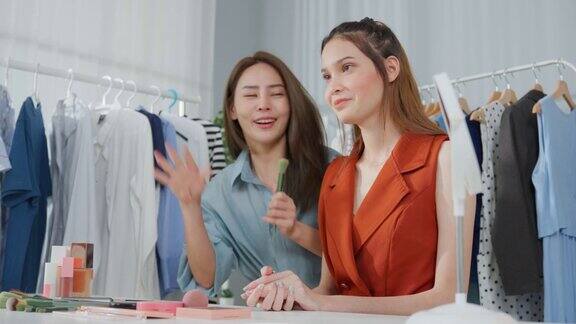 亚洲两名女性视频博主对着镜头回顾在家里的美容美妆博主网红女性朋友在办公室商店的平板电脑上直播并展示化妆刷