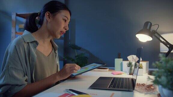 年轻的自由亚洲妇女使用笔记本电脑视频会议电话会议在家里的客厅晚上