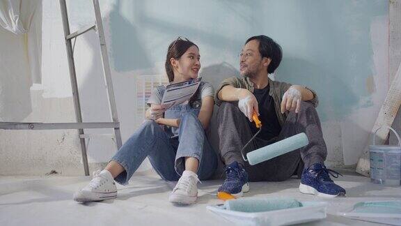 一对亚洲夫妇在粉刷房子的墙壁休息时正在聊天