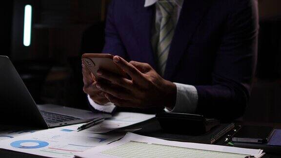 商人使用现代笔记本电脑和智能手机在办公桌上分析商业财务文件商人在办公室的办公桌上使用手机