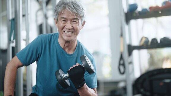 亚洲华人高级男子健身哑铃在健身房看着镜头微笑