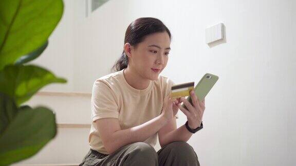 坐在楼梯上用智能手机和信用卡在家里网购的亚洲女性