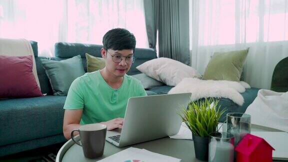 4K一个年轻的亚洲人的特写穿着绿色衬衫低头看着他的笔记本电脑对他的工作有一个严肃的表情在房子里