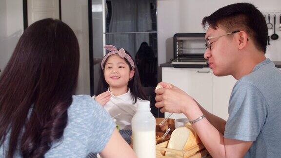 日本亚裔家庭在家里吃早餐亚洲的妈妈爸爸和女儿感到愉快的谈话在一起吃面包玉米片谷物和牛奶碗在厨房的桌子上在早上
