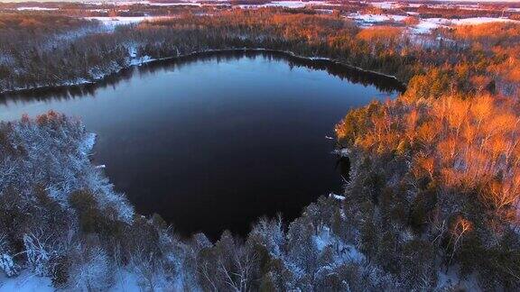 晨曦中冰雪覆盖的树林环绕着结冰的湖面